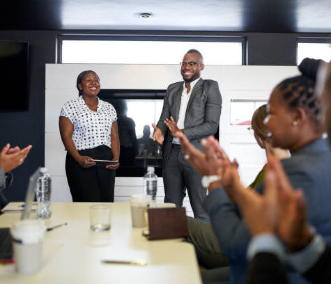 Group of mixed race colleagues in modern meeting room with laptop computer encouraging two attractive African American business professionals leading a collaborative discussion